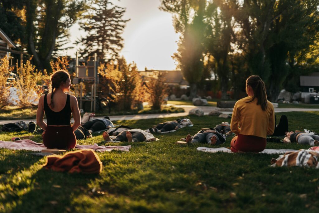 Two women sitting amongst other laying in a yoga class. 